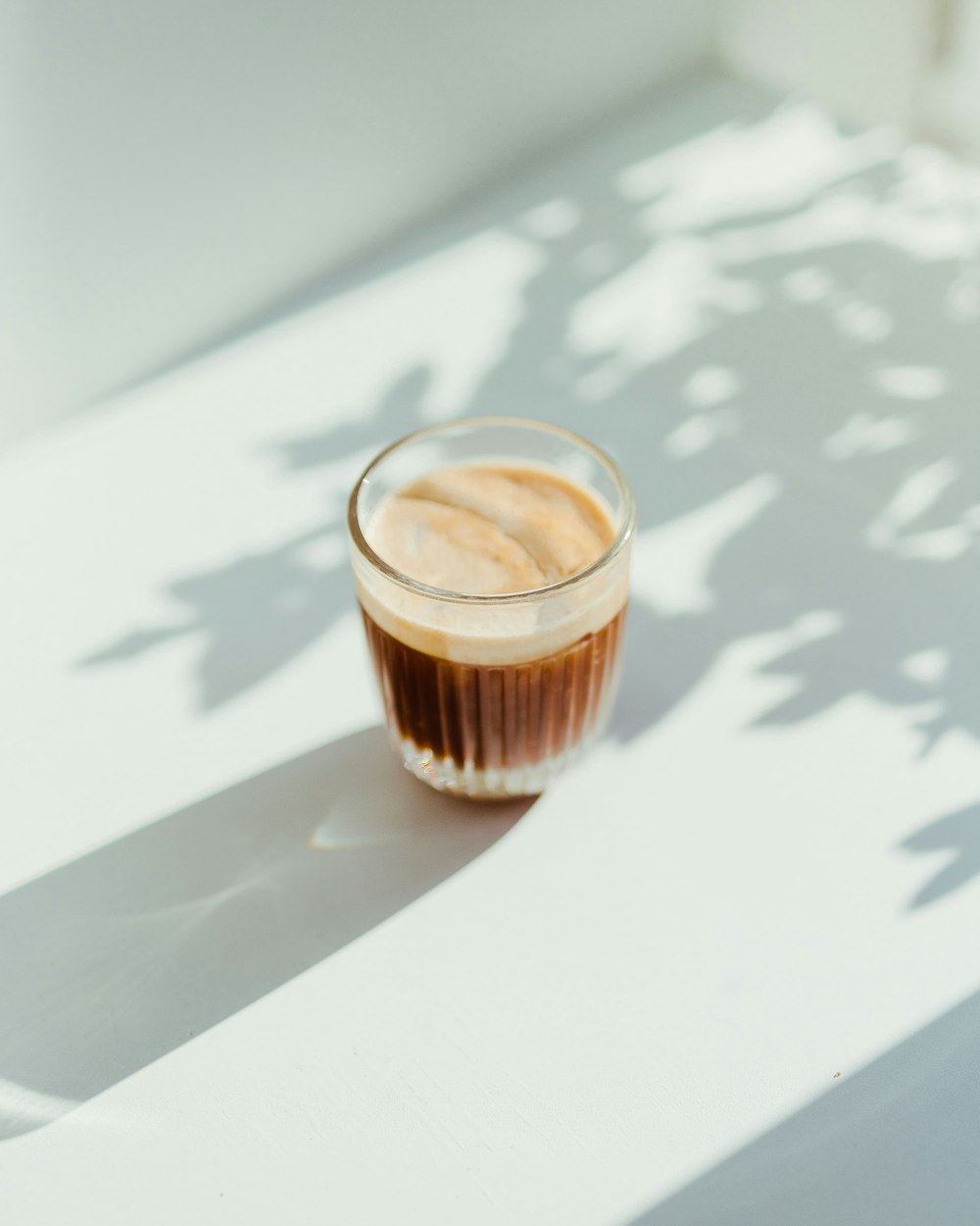 Klares Trinkglas mit Kaffee auf weißem Tisch