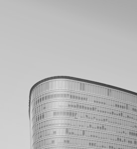 A sleek modern office building with a rounded, glass exterior reflecting a minimalist design. The building features horizontal bands of windows and smooth curves that give it an elegant appearance against a clear sky background.