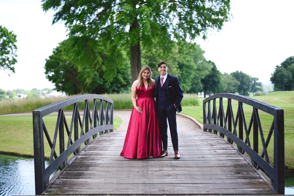 man and woman wearing formal attire standing on wooden bridge