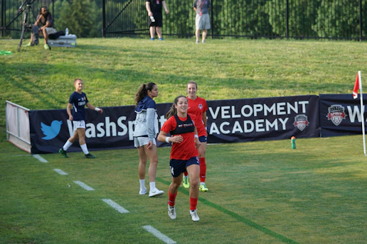A cheerful soccer mom cheering from the sidelines with a vibrant soccer field in the background.