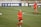 Two female soccer players are on a soccer field wearing red and dark blue uniforms. One player is in the foreground running with a green headband and the number 31 on her shorts, while the other player is in the background. The field has markings and soccer balls are scattered around. Advertising banners with social media icons and text are visible in the background.