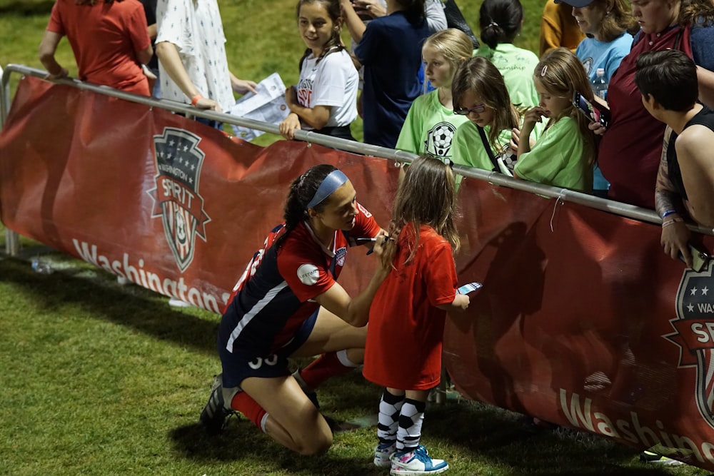 woman wearing red and black jersey helping little girl