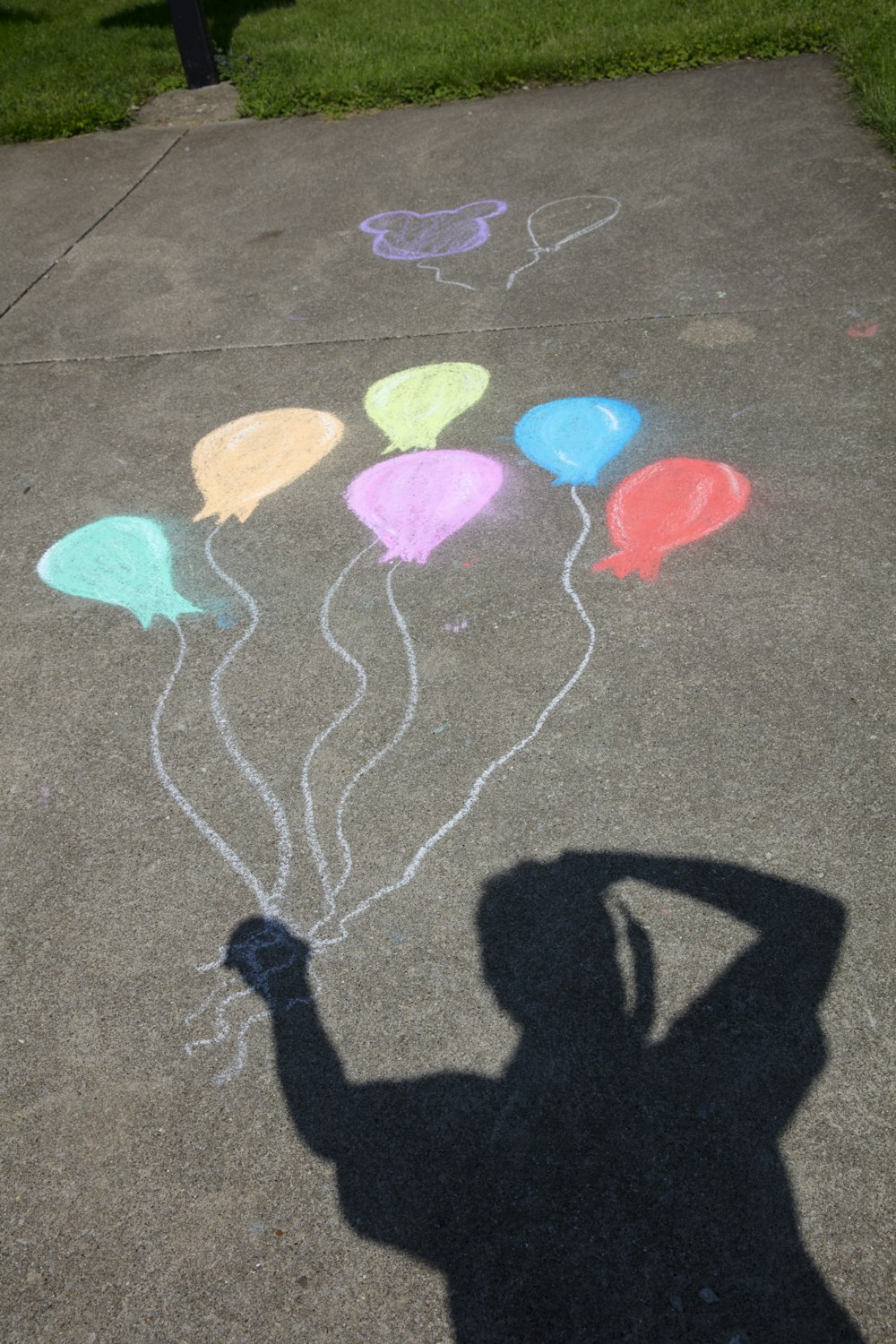 person's shadow holding bundle of balloons chalk art on concrete ground