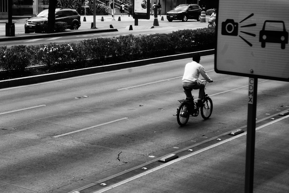 grayscale photography of person riding bike on road