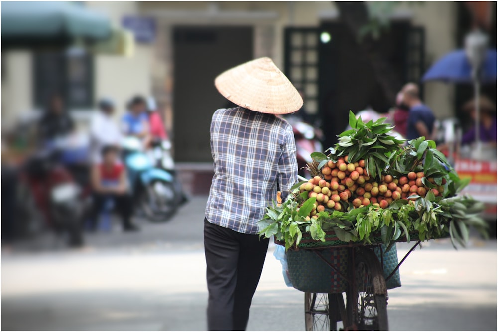 person wearing brown straw hat carrying black bike with vegetables
