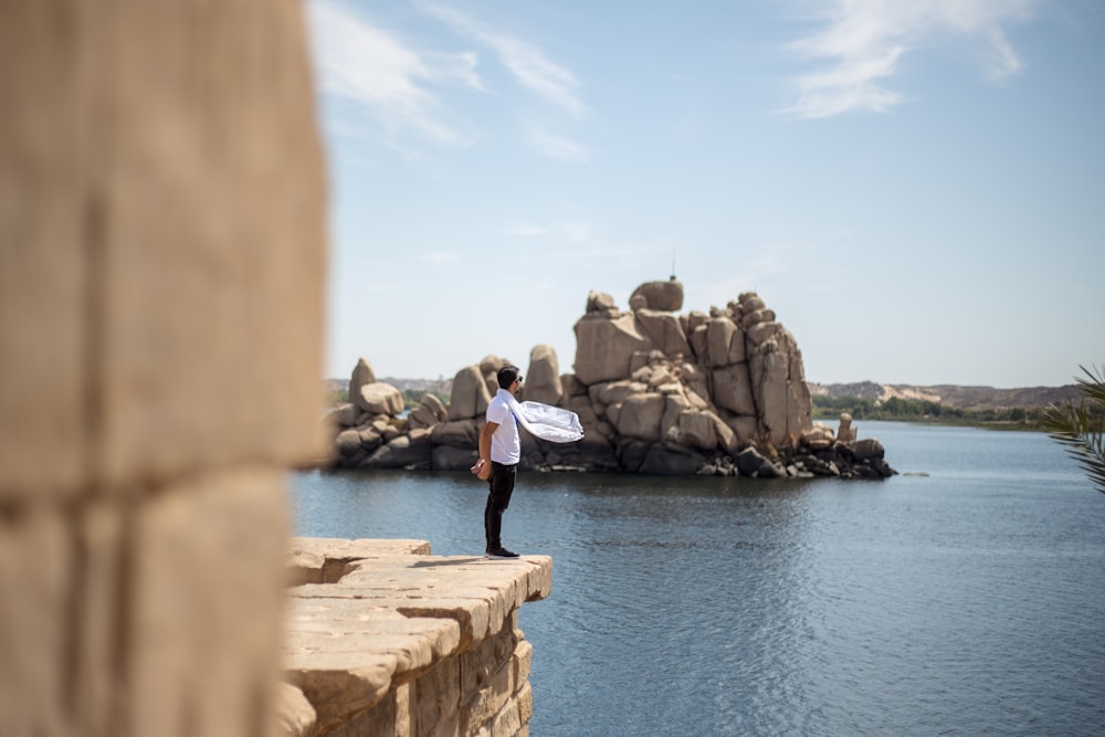 man standing on brown cliff towards body of water