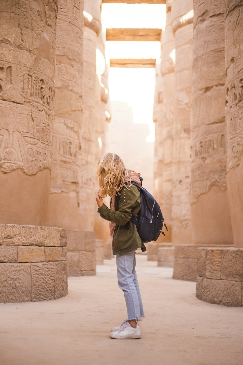 woman in brown jacket standing near brown concrete pillars