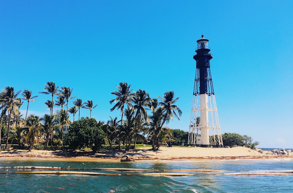 white and black tower beside sea and trees during daytime