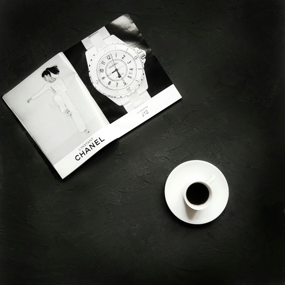 grayscale photography of cup and saucer near papers