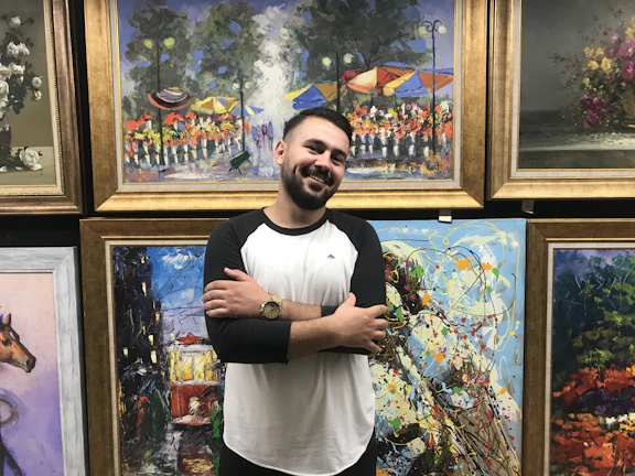 A smiling artist standing proudly beside a vibrant, abstract painting.