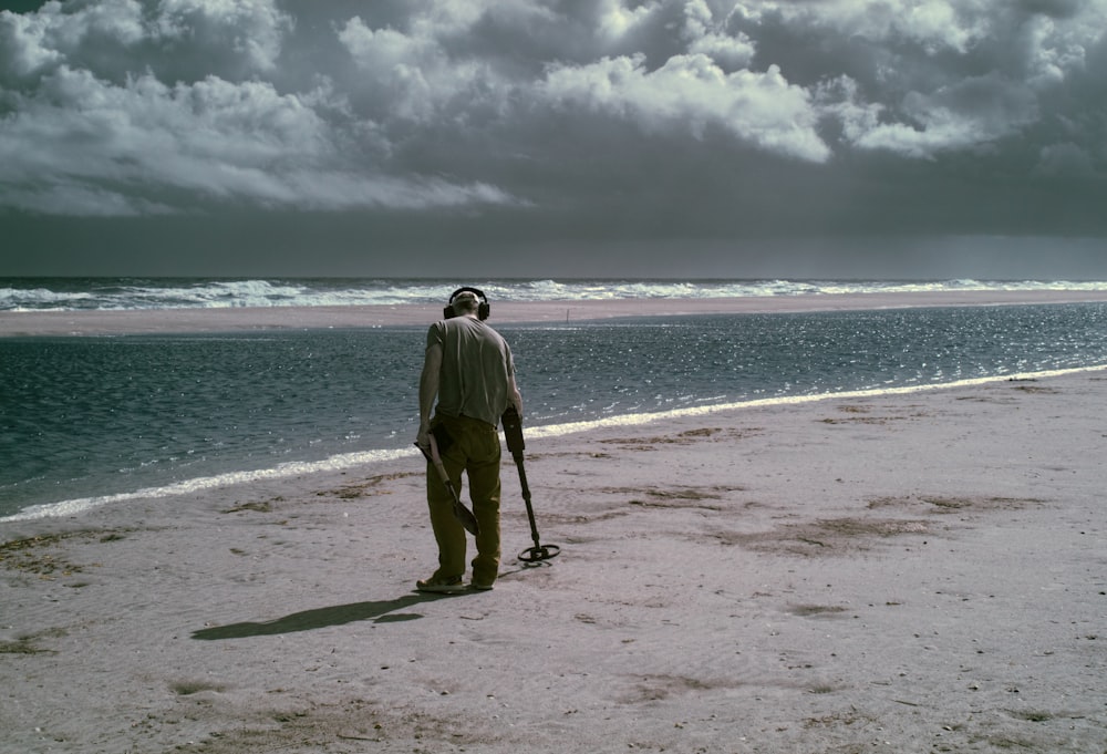 man using metal detector at the shore during day