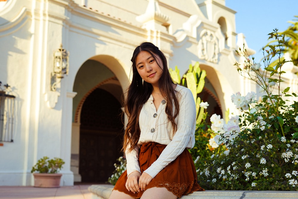 woman in white top and brown shorts sitting outside building