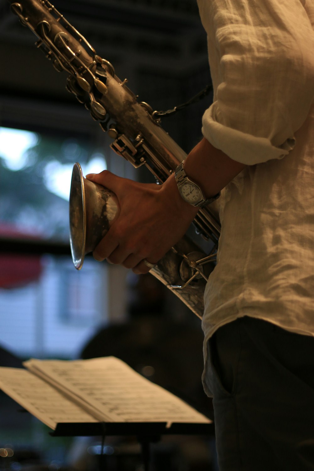 man in white dress shirt holding saxophone in front of music sheet on stand