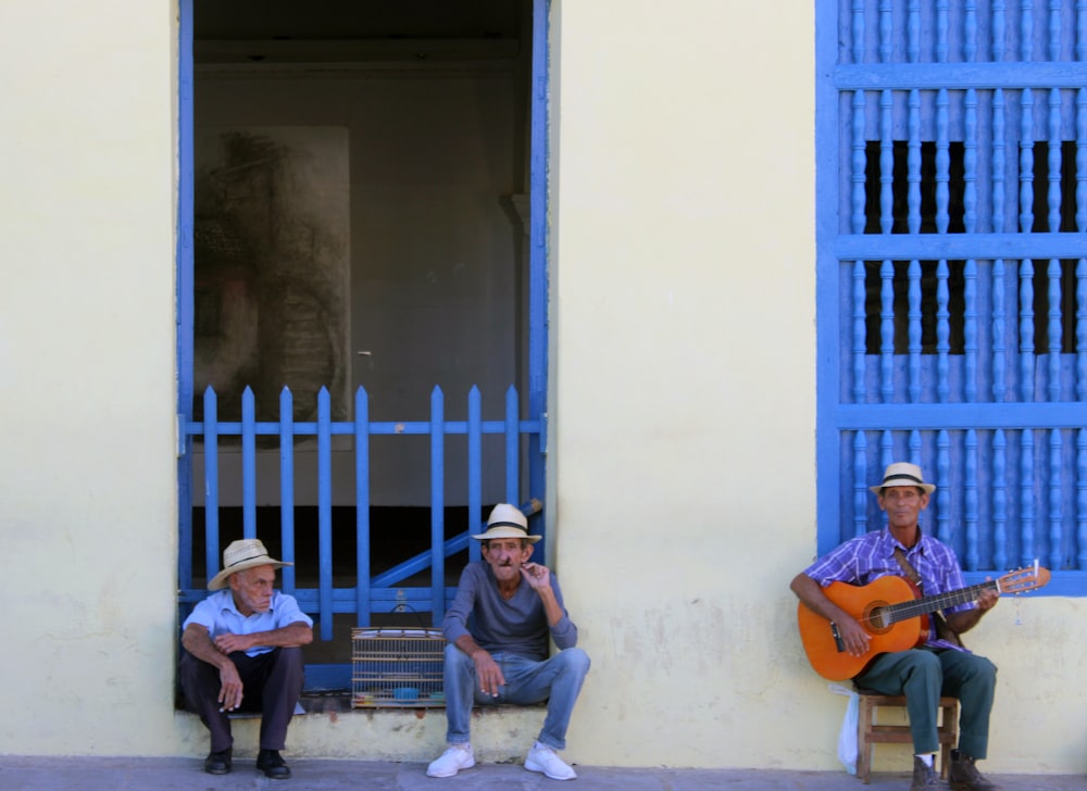 three men sitting near white building