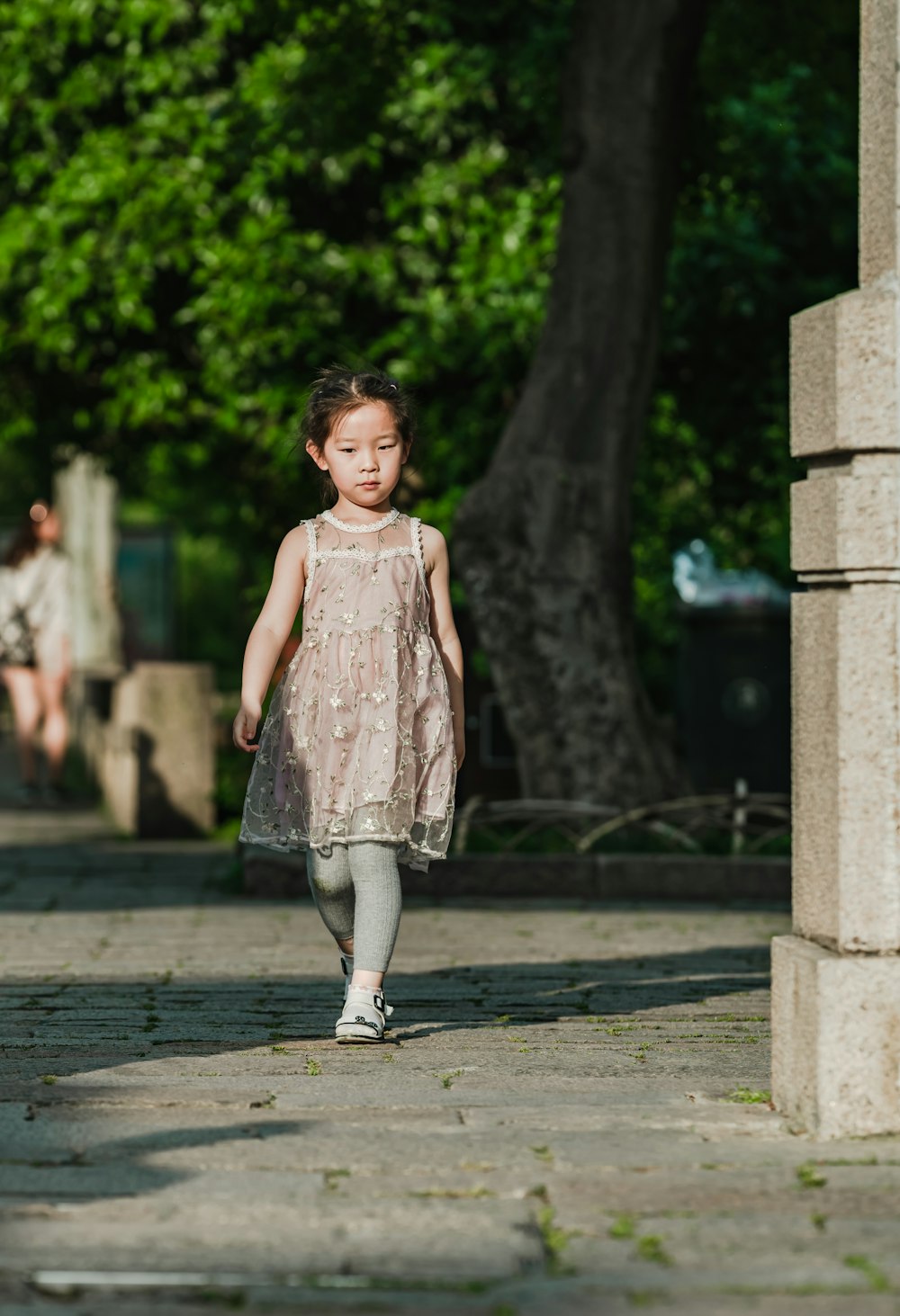 Muchacha caminando por un camino de cemento cerca de un árbol