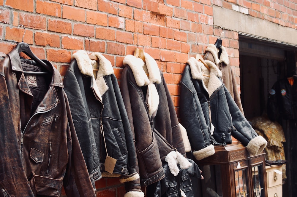 four assorted leather jackets hanging on brown brick wall