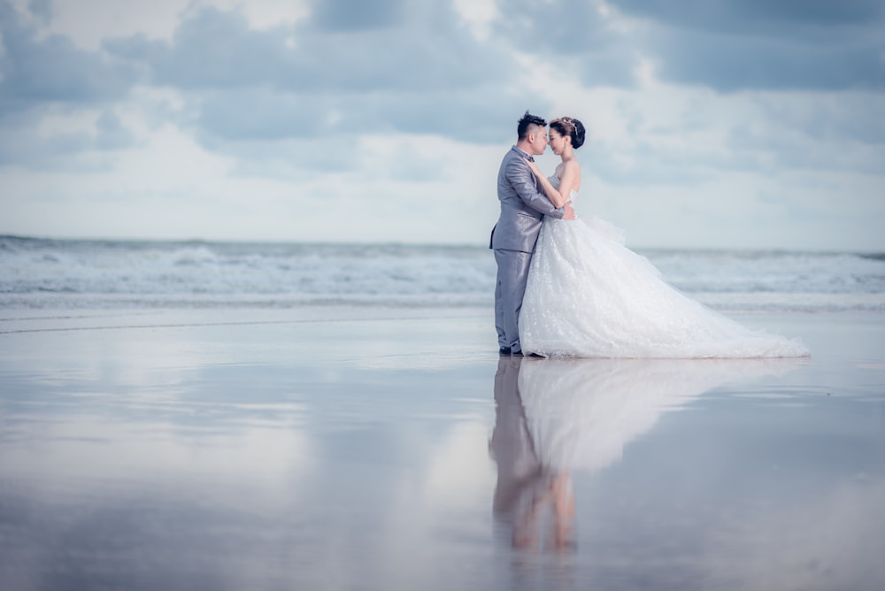 man and woman wearing wedding dress standing on seashore