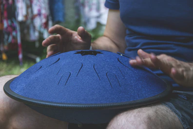 Close-up of hands playing a handpan, highlighting the instrument's smooth metallic surface and warm tones.