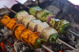Freshly made paneer tikka skewers sizzling on a grill with charred edges and vibrant spices.