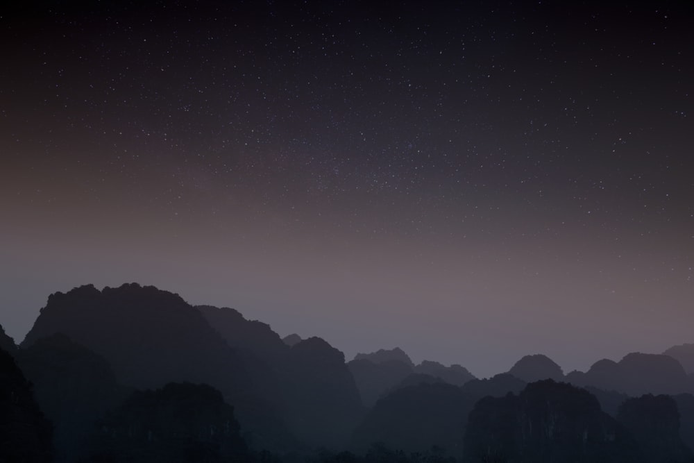 a night sky with stars and mountains in the background