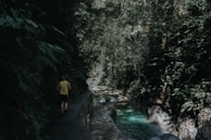 man walking beside river near mountain during daytime