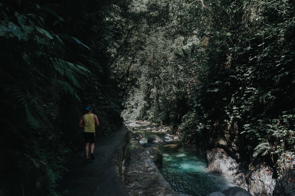 man walking beside river near mountain during daytime