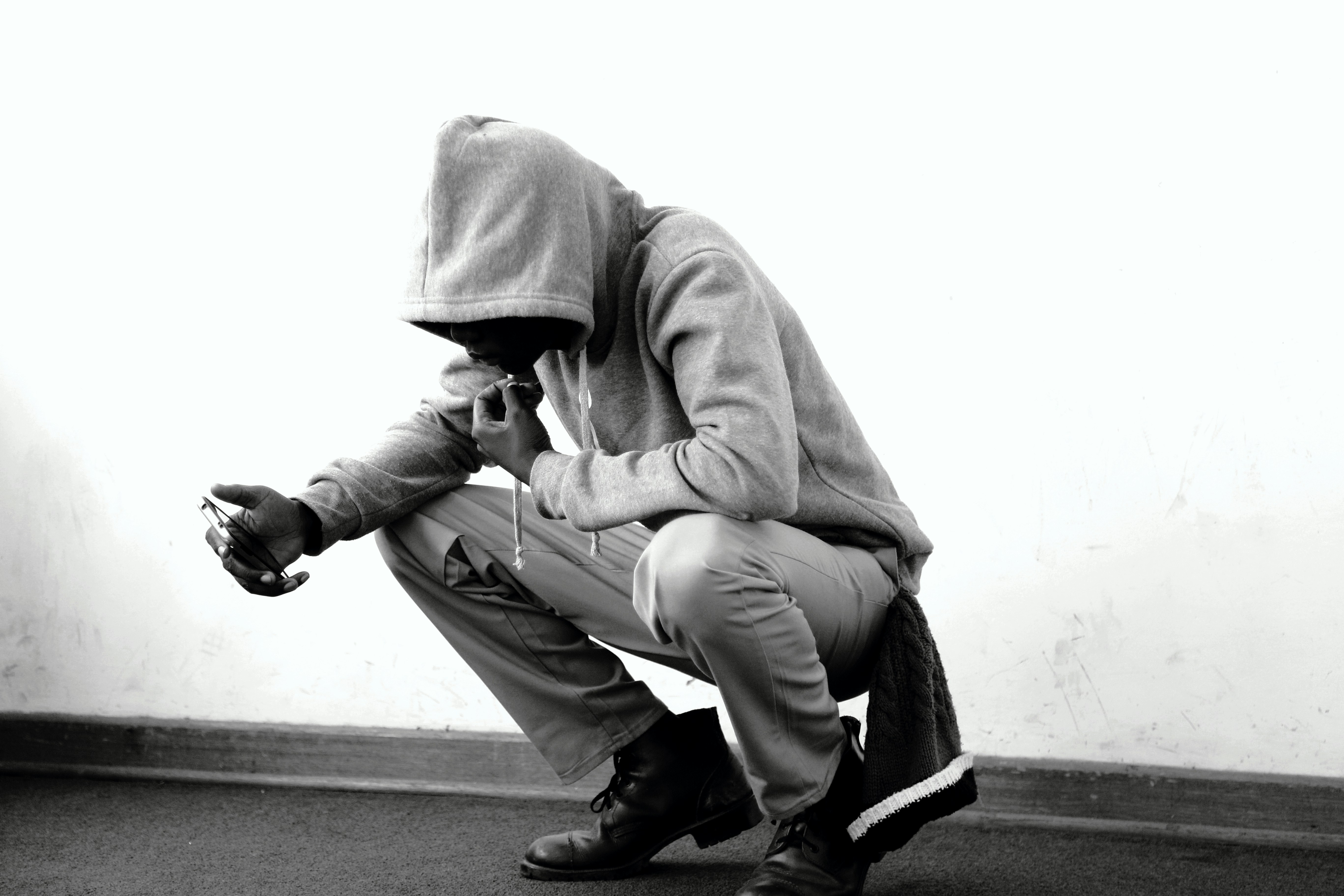 man in grey hoodie and pants sitting beside white wall