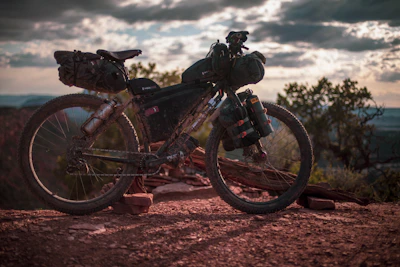 A rugged adventure bike standing tall on a rocky trail with a sunset backdrop.