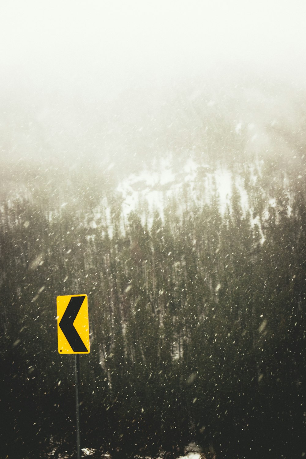 a yellow sign sitting on the side of a snow covered road