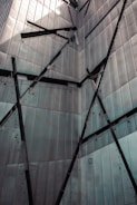A building facade with angular, intersecting metal panels and bolts, creating a geometric and industrial appearance.