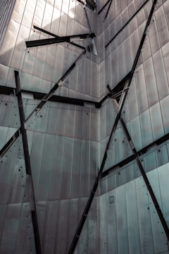 A building facade with angular, intersecting metal panels and bolts, creating a geometric and industrial appearance.