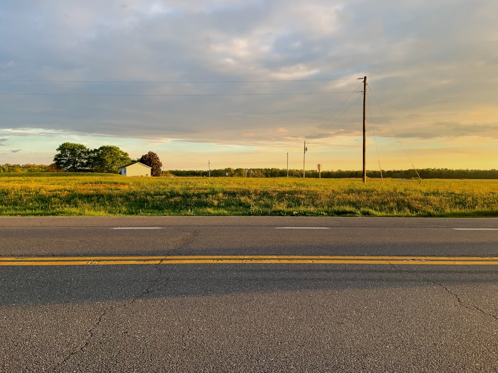 gray paved road beside green grass field