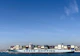 A large cargo ship with the name 'COSCO SHIPPING' is carrying numerous stacked shipping containers on calm blue waters. The background shows a distant coastline under a clear, blue sky.