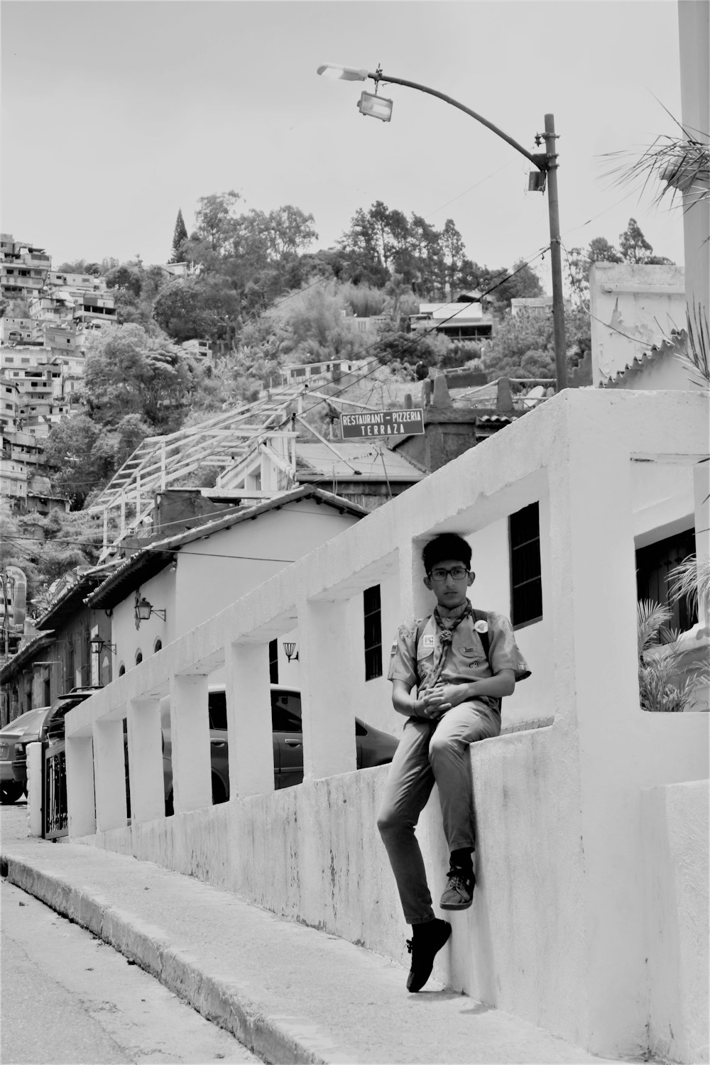 grayscale photo of boy sitting on concrete balustrade