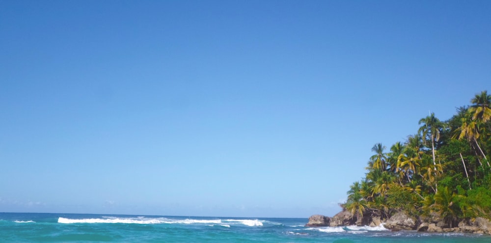 photography of ocean waves beside mountain during daytime