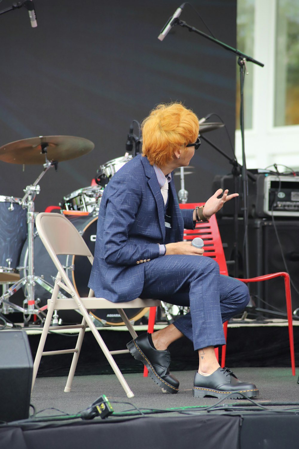 man wearing suit sitting on folding chair while holding microphone