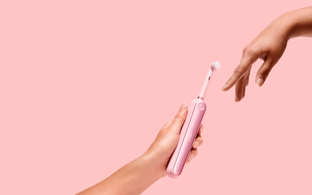 pessoa segurando escova de dentes elétrica rosa
