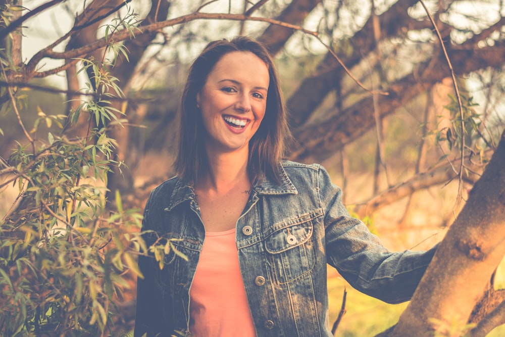 Frau trägt blaue Jeansjacke hinter Baum