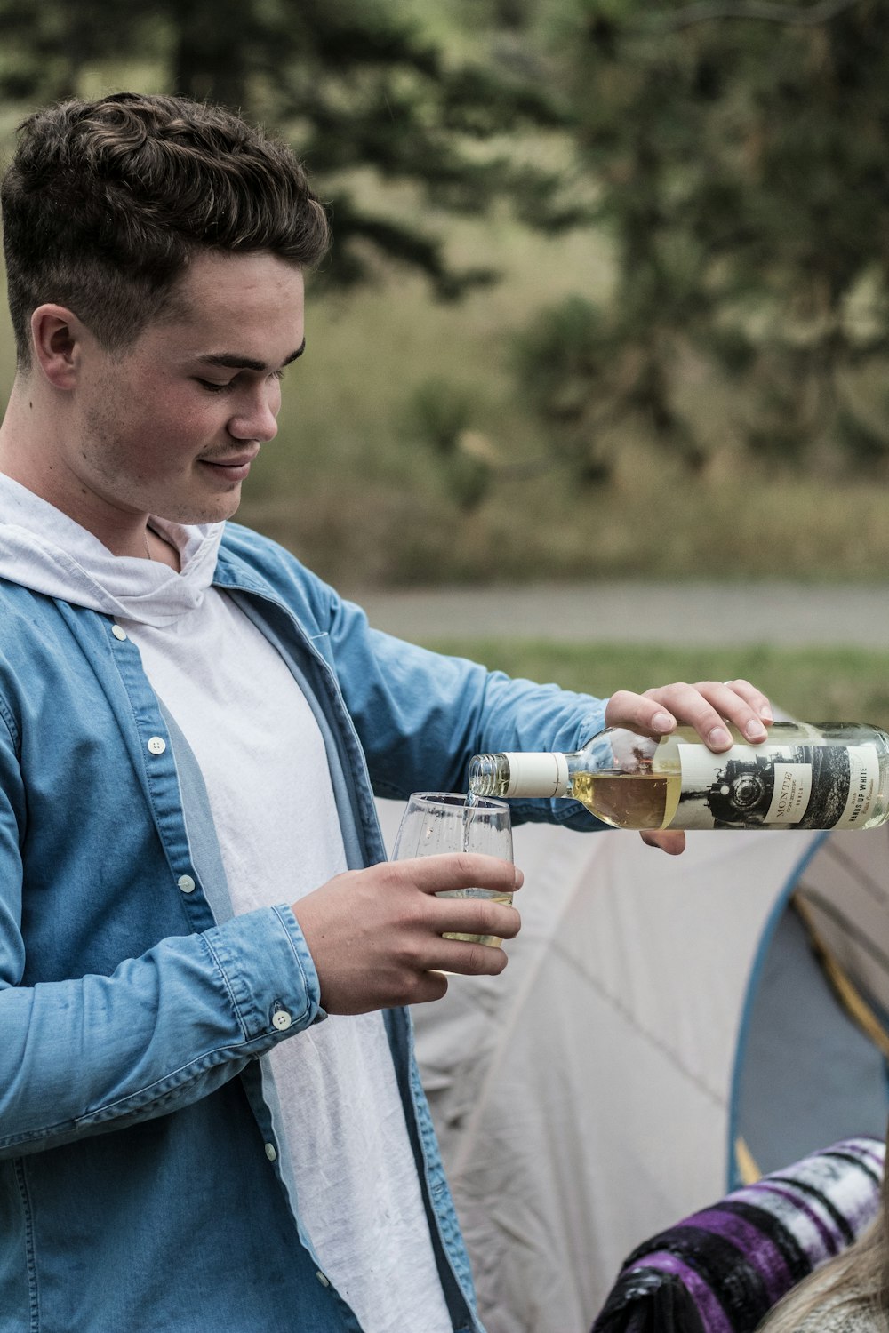 man wearing blue denim jacket holding bottle and rock glass