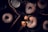 A variety of powdered sugar-covered donuts are displayed on a black surface. Some are placed on a cooling rack, while others are inside a wooden box. A broken donut reveals its soft, golden interior. A metal sifter is nearby, suggesting the process of sprinkling the sugar.