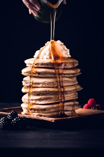 An overhead shot of a syrup bottle of flavvafull next to pancakes topped with fresh berries and syrup drizzle.