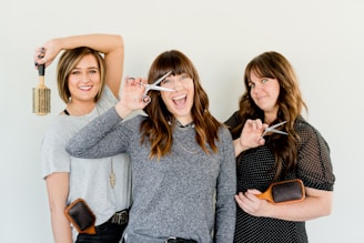 three women holding scissors and brush