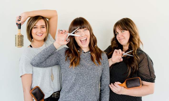 three women holding scissors and brush