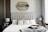 A well-designed bedroom featuring a large upholstered bed with a tufted headboard. The bed is adorned with textured and patterned pillows. On either side of the bed are wooden nightstands, each holding a silver lamp. Above the bed is an ornate mirror with a gold frame. Decorative geometric accents and a soft gray throw blanket complete the room's elegant and cozy atmosphere.