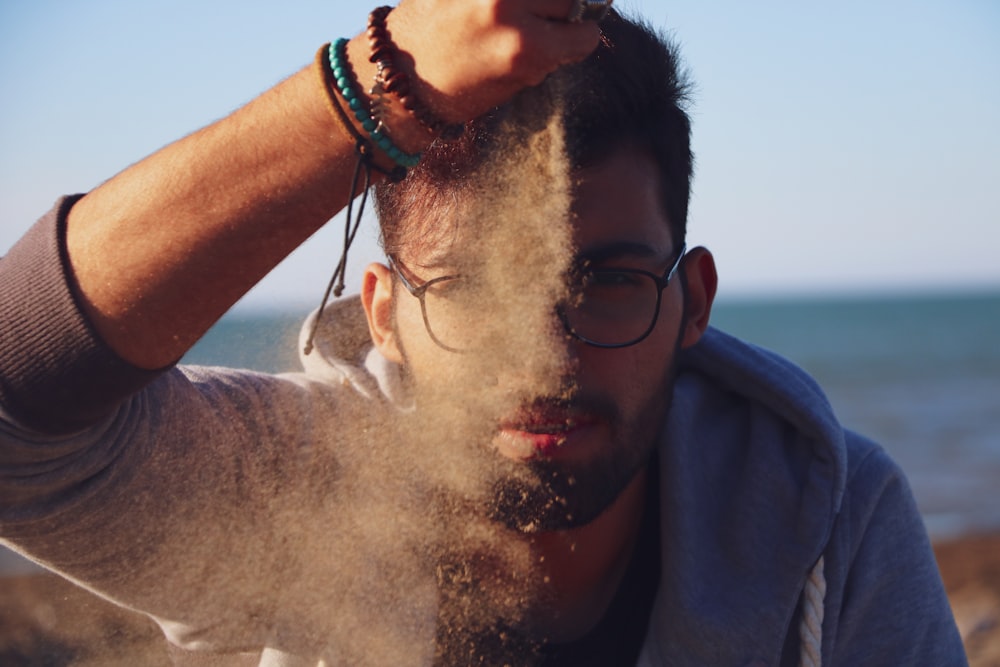 man wearing gray hoodie with sand on hand