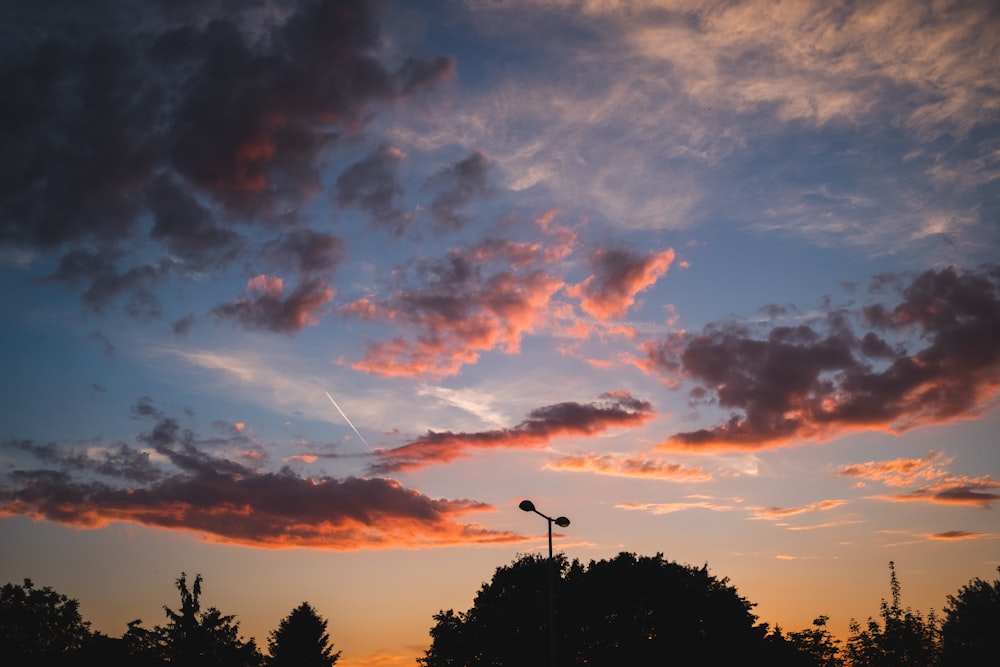 a sunset with clouds and a street light in the foreground