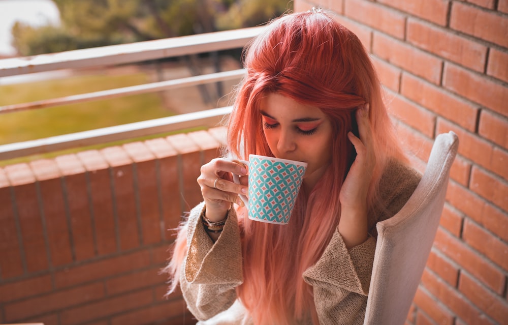 woman wearing beige trench coat holding teal ceramic mug