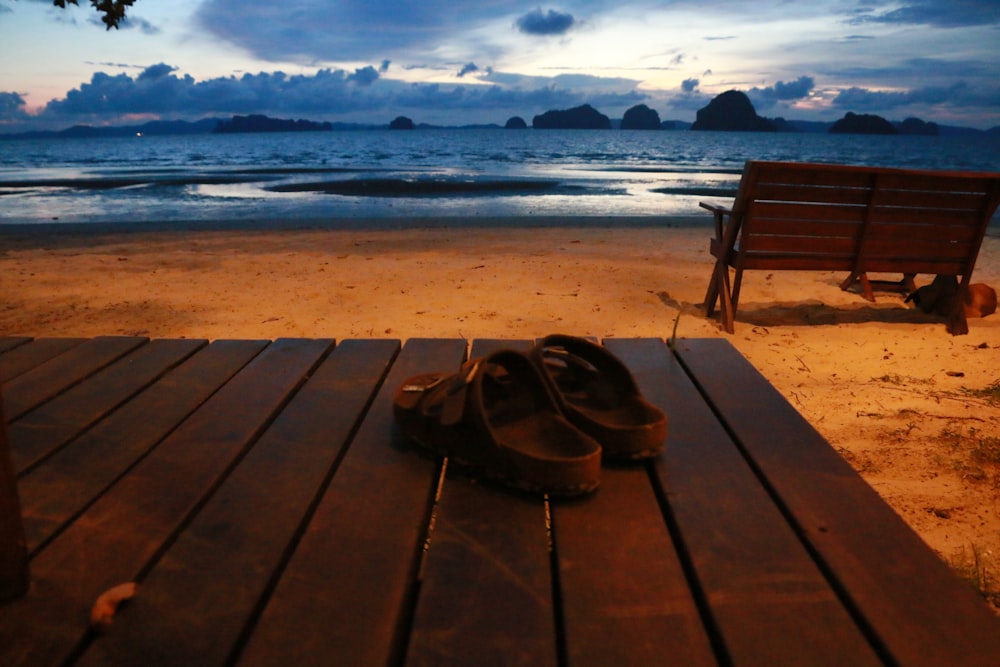 sandals on wooden table near bench facing the ocean during golden hour