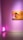 A minimalistic art gallery room with pink walls features a framed artwork of a stylized figure in warm colors, predominantly oranges and pinks. Near the corner, a neon light sculpture resembling an ice cream cone glows in bright pink.