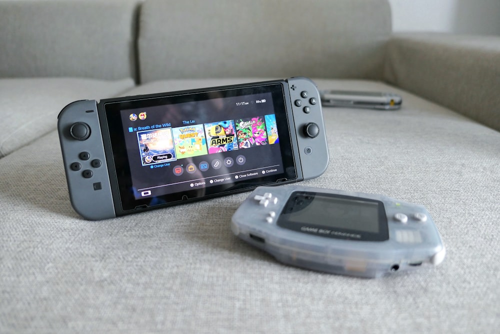 two black Nintendo Switch console turned on beside Nintendo Game Boy Advance console on sofa